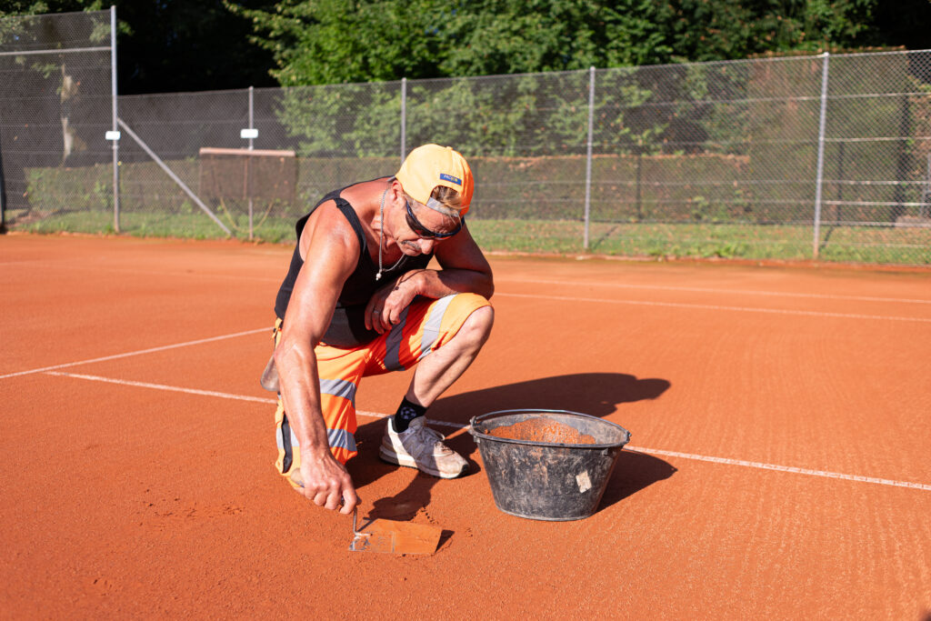 Mitarbeiter des Läbesruums bessert den Boden eines Tennisplatzes aus.