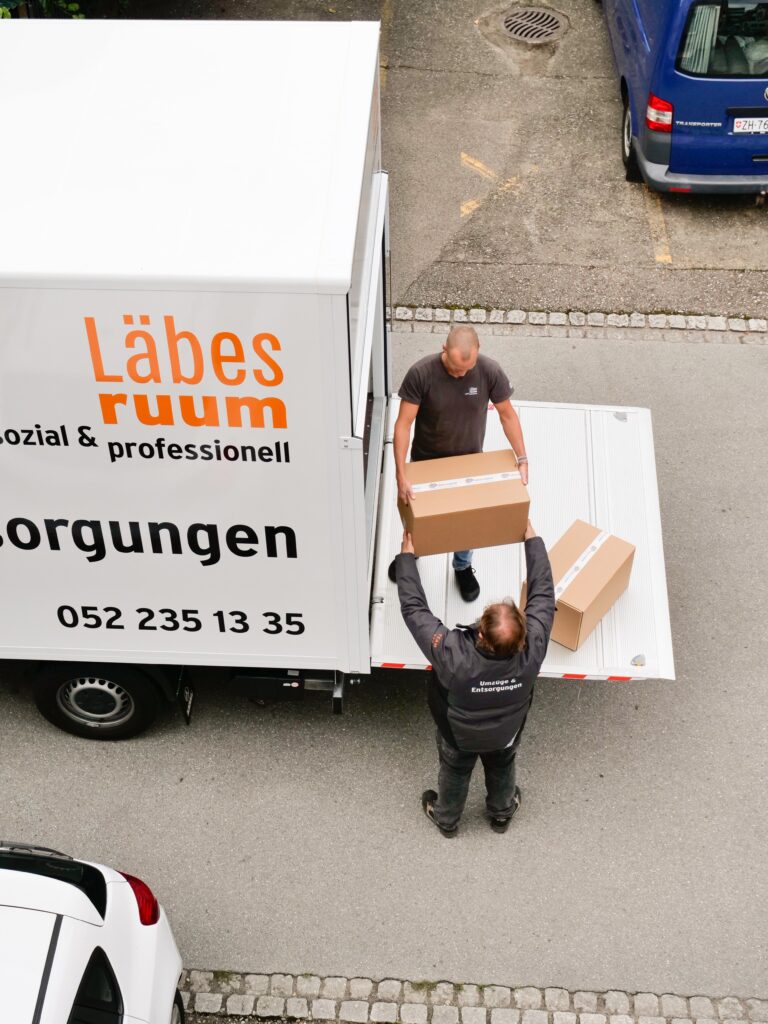 Zwei Mitarbeiter des Läbesruums tragen Umzugskartons in einen Lastwagen.