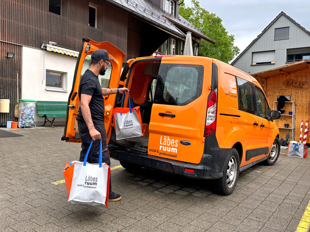 Ein Mitarbeiter des Läbesruums trägt gefüllte Recyclingtaschen in ein Auto.