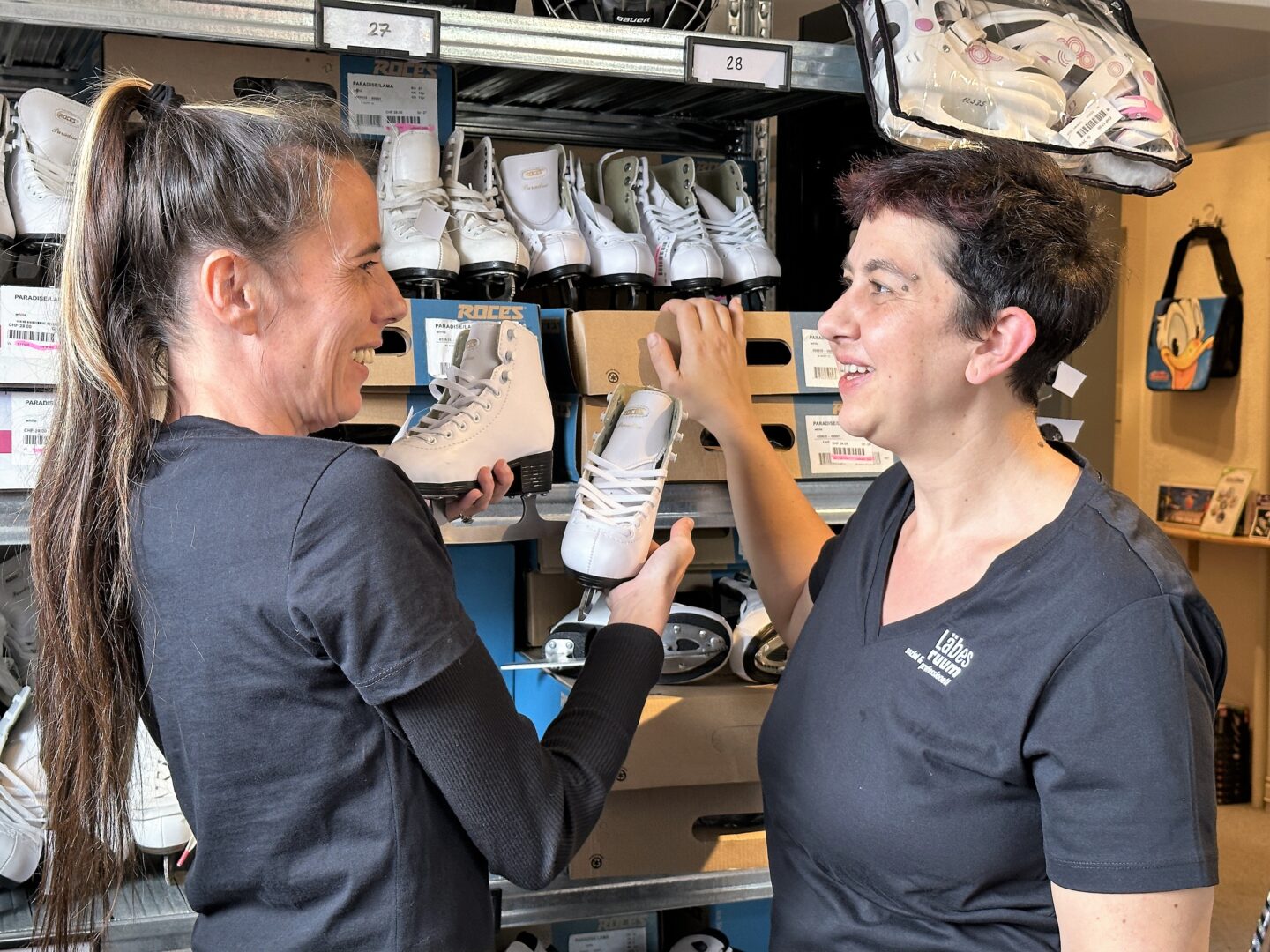 Zwei Mitarbeiterinnen der Läbesruum Spiel- & Sportbörse vor einem Regal mit Schlittschuhen.