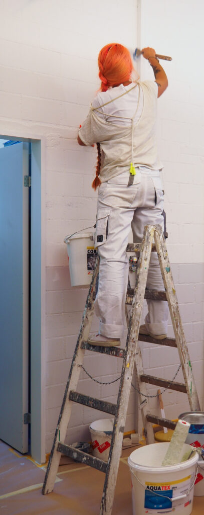 Eine Mitarbeiterin des Läbesruums streicht eine Wand neu an.