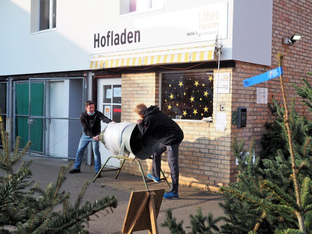 Zwei Mitarbeiter des Läbesruums verpacken einen Tannenbaum.
