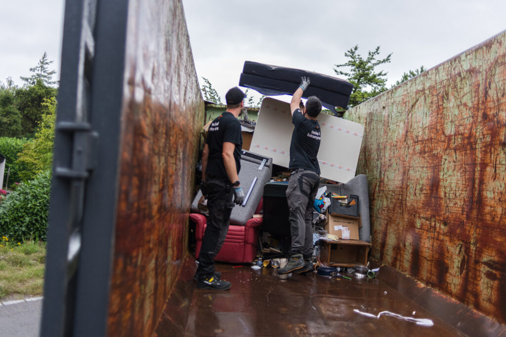Zwei Mitarbeiter des Läbesruums entsorgen bei einer Räumung Hausrat in einer Mulde.