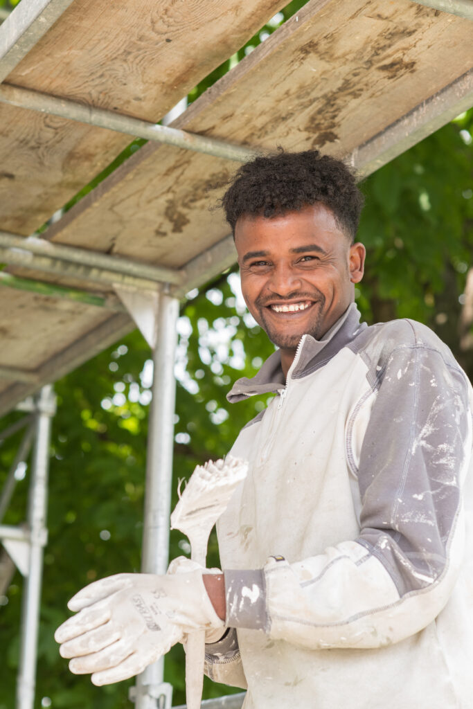 Ein Lernender des Läbesruums auf einem Baugerüst um eine Fassade zu malen.