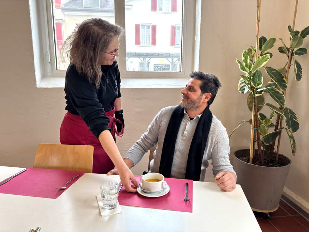 Mitarbeiterin des Läbesruums serviert einem Gast einen Teller Suppe.