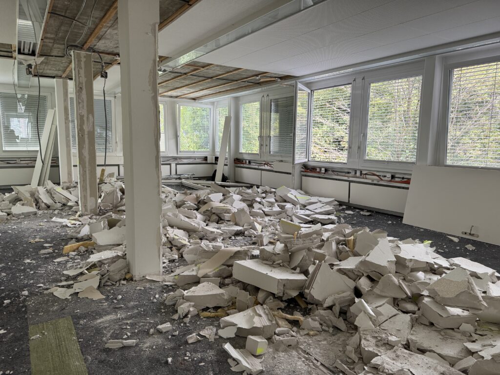 Blick in eine Baustelle, wo gerade Zwischenwände abgebrochen werden. Es liegt sehr viel Schutt herum.